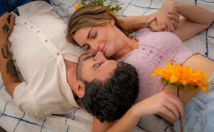 Couple lying on picnic blanket surrounded by yellow flowers.