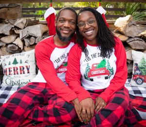 Family wearing matching Christmas pajamas poses on blanket with holiday decorations.