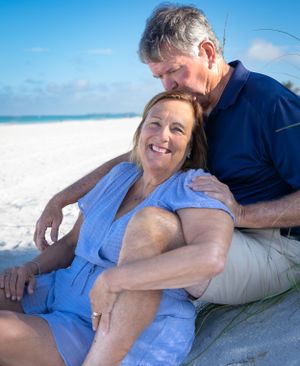 Couple lounges together on sunny beach with white sand and blue skies.