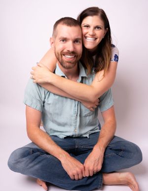 Couple in casual denim and blue sitting together in a studio against white background.