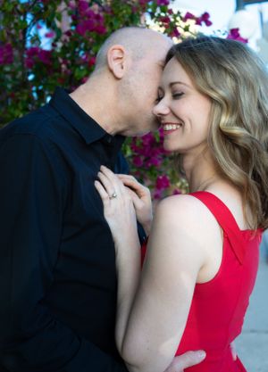 Romantic couple sharing tender moments against backdrop of purple bougainvillea flowers.