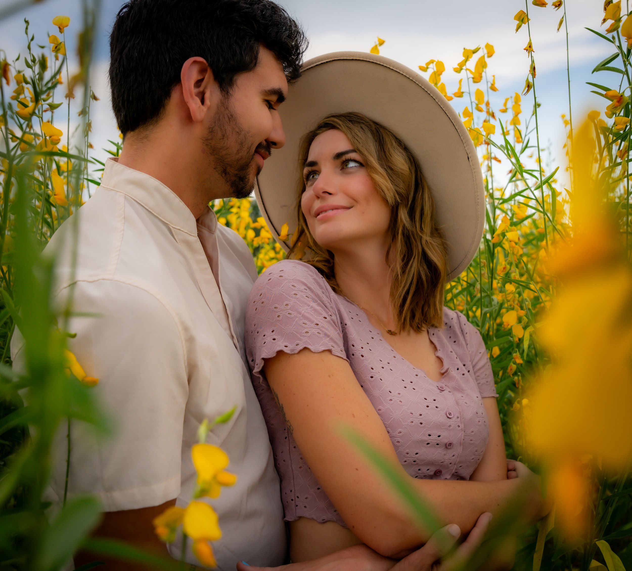 Romantic couple pose among yellow wildflowers during outdoor photo session.