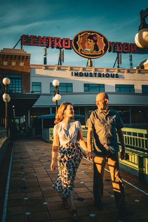 Couple shares romantic moment at sunset on rooftop with city lights and vintage neon signs in background.