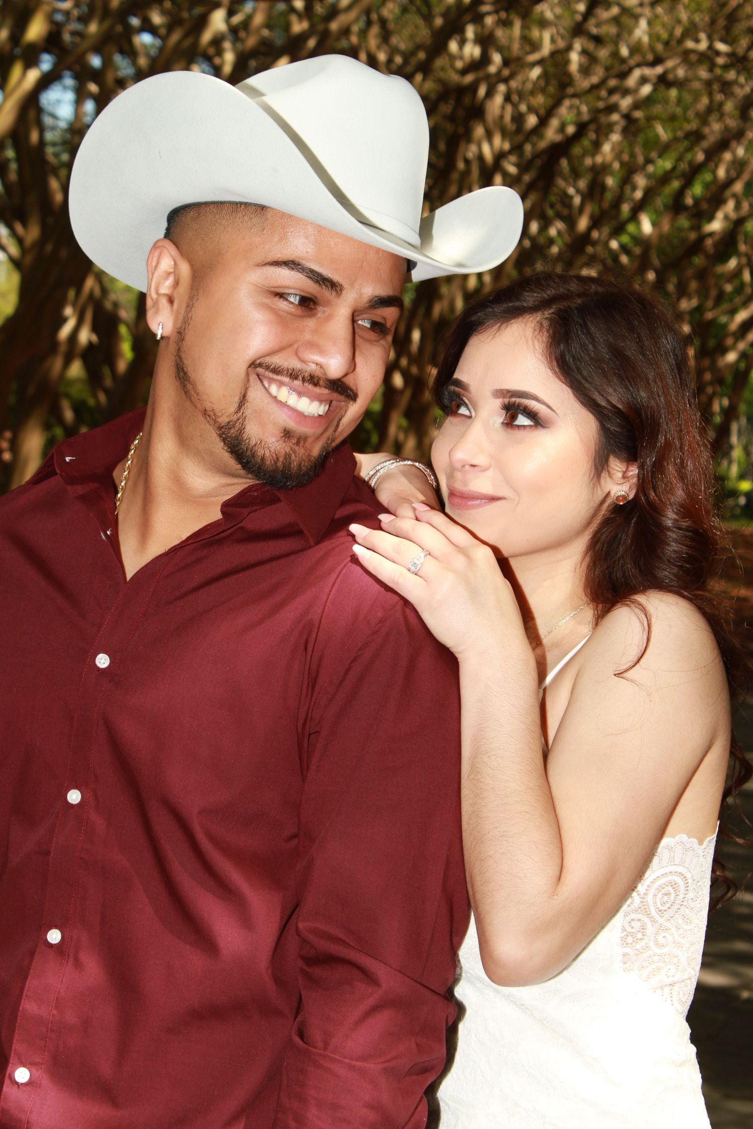 A couple in burgundy and white attire share an intimate moment outdoors.
