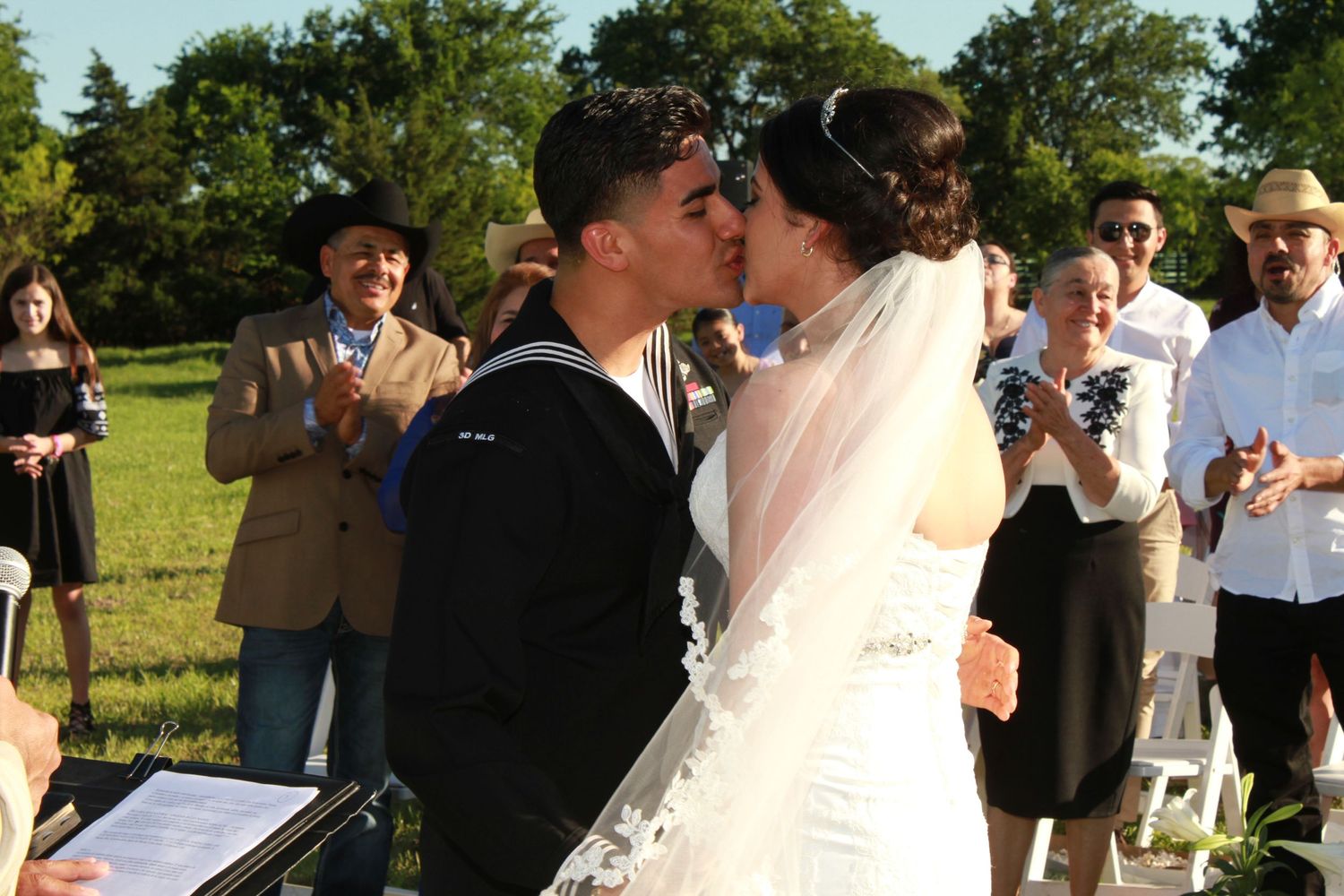 Wedding guests celebrate at an outdoor ceremony with trees in the background.