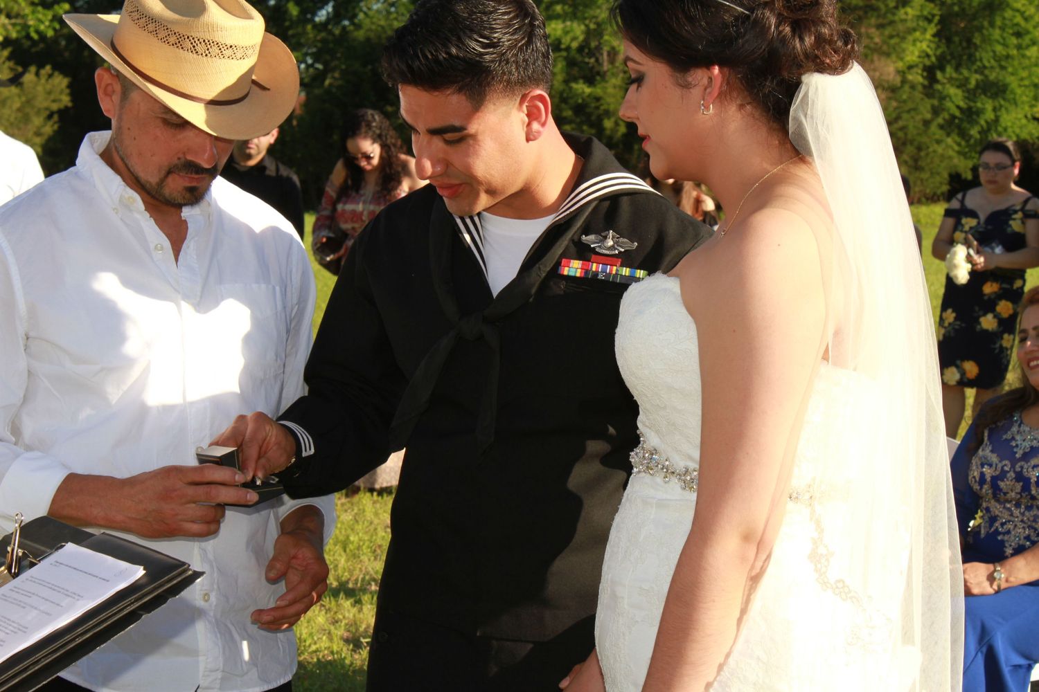Outdoor wedding ceremony taking place under blue skies with guests gathered around.