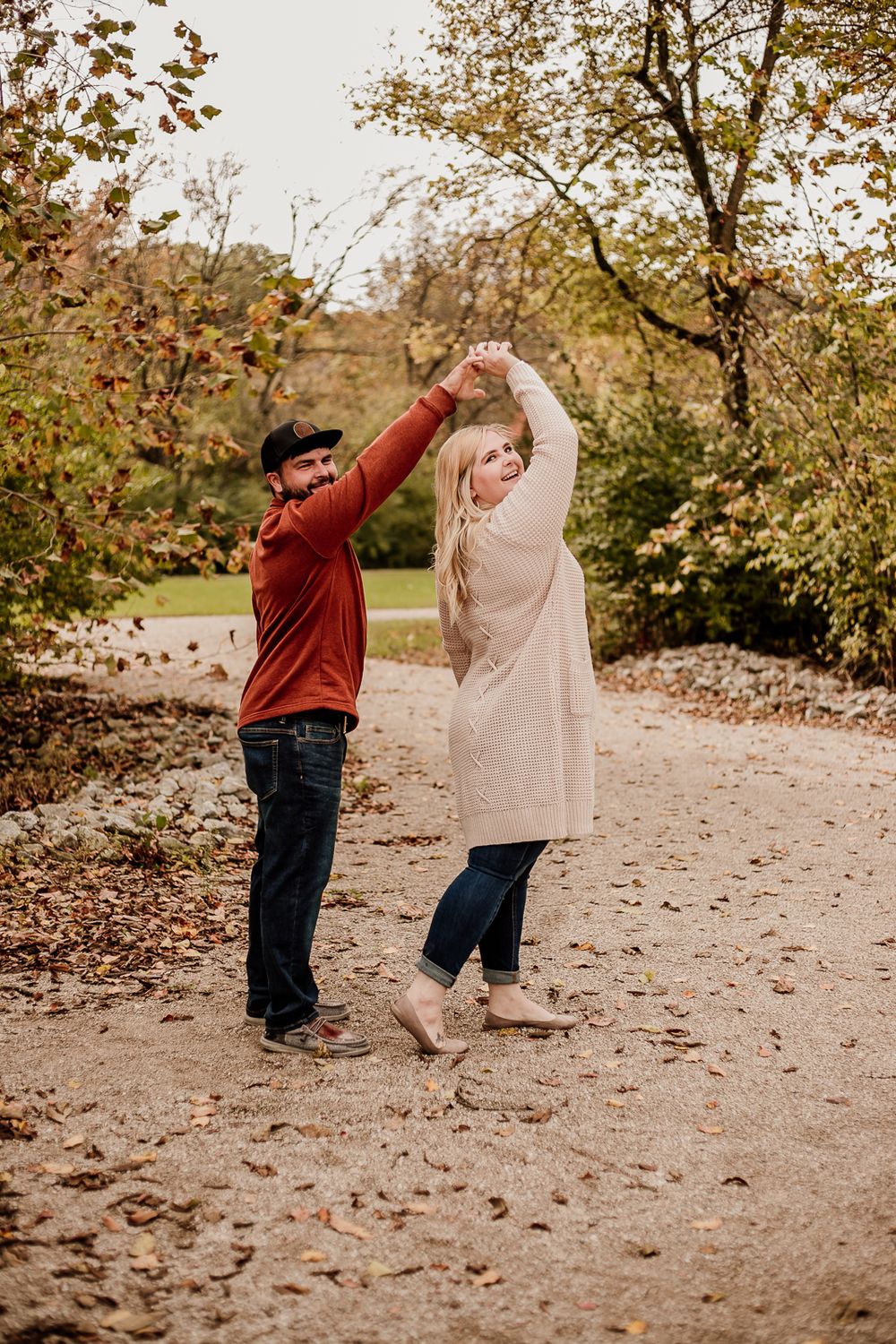 Two people dancing and twirling on a leaf-covered path during autumn photoshoot.