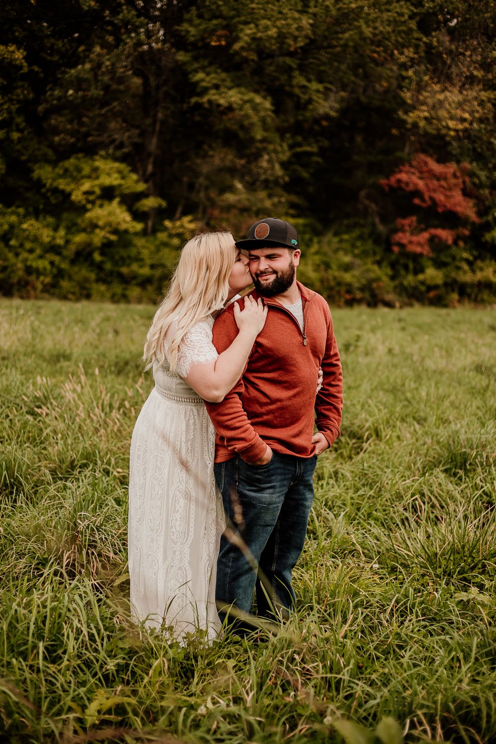 Couple sharing tender moments in field with autumn foliage in background.