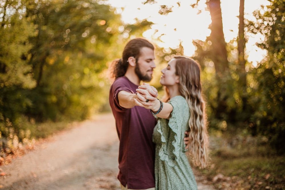 A couple shares a romantic moment on a sunlit forest path during golden hour.