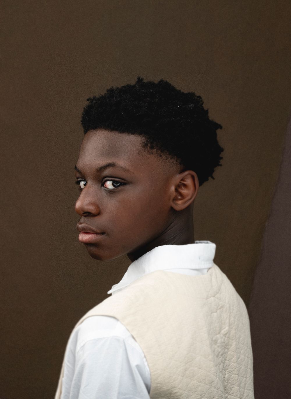Professional portrait of a young person in white clothing against a brown backdrop.