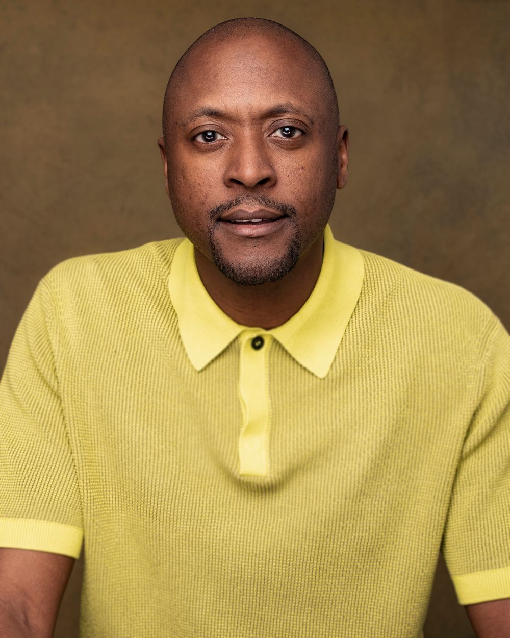 Portrait of a person wearing a yellow polo shirt against a brown background.