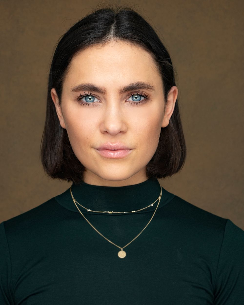 Studio portrait of person in dark green top with delicate gold necklaces.