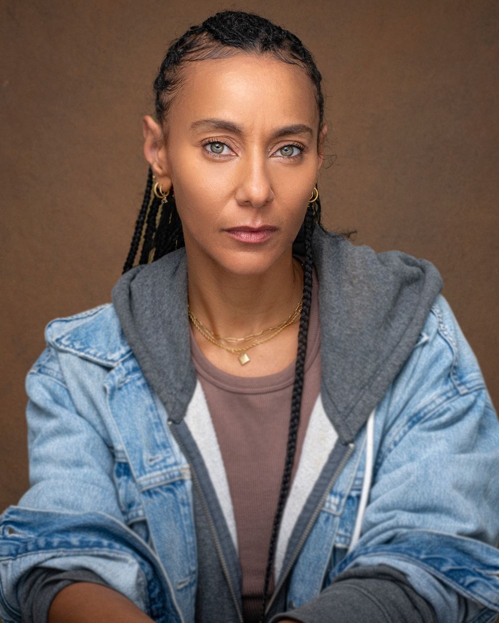 Studio portrait featuring braided hair, denim jacket and layered necklaces.
