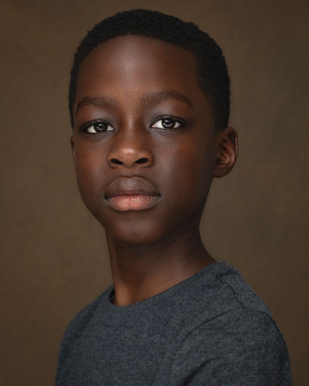 Studio portrait of young person in gray t-shirt against brown background.