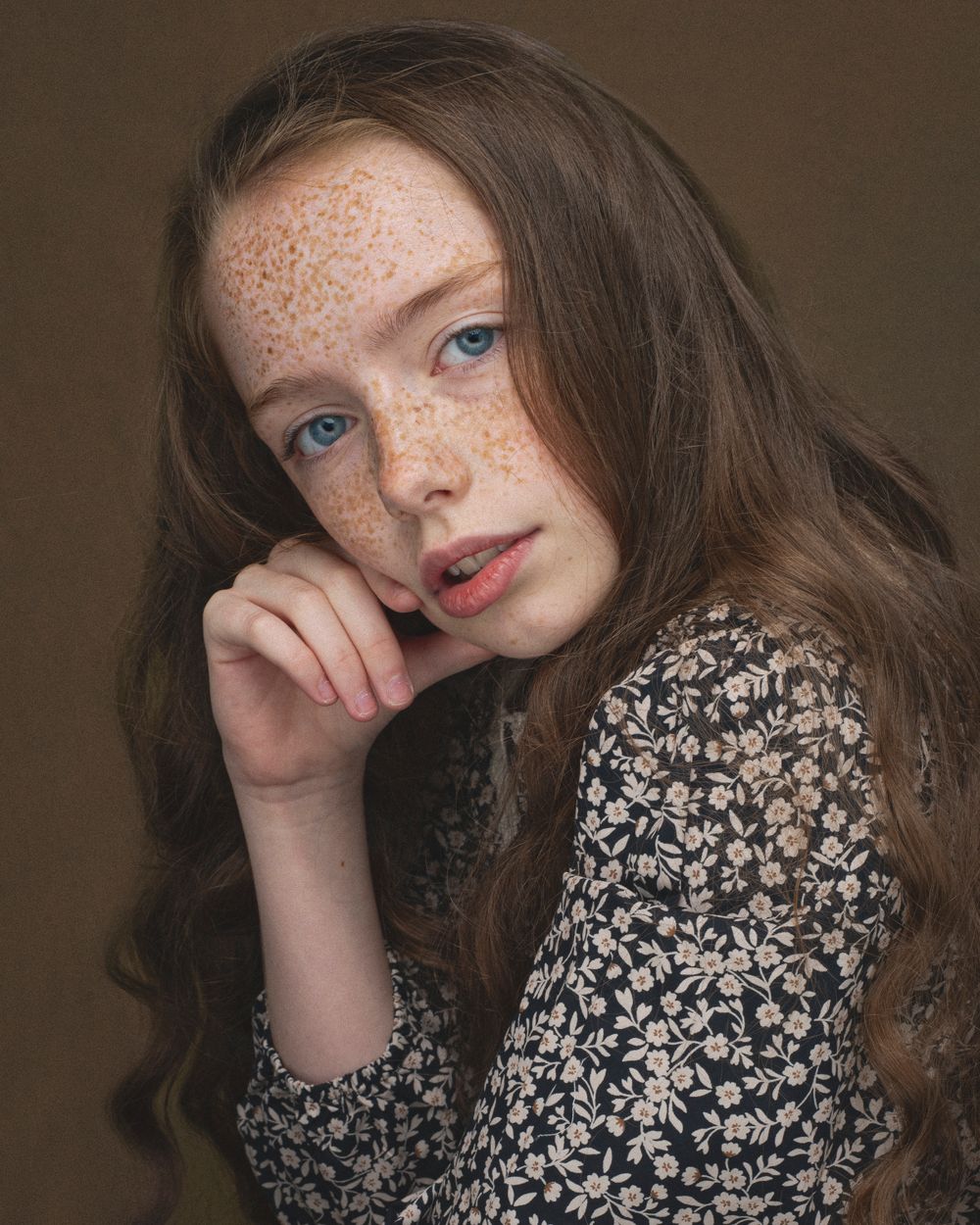 Portrait showcasing natural freckles and long brown hair against a dark background.