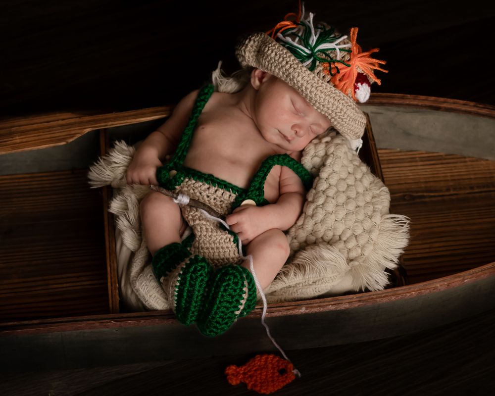 Baby wearing knit costume with green and orange details lying in wooden prop.
