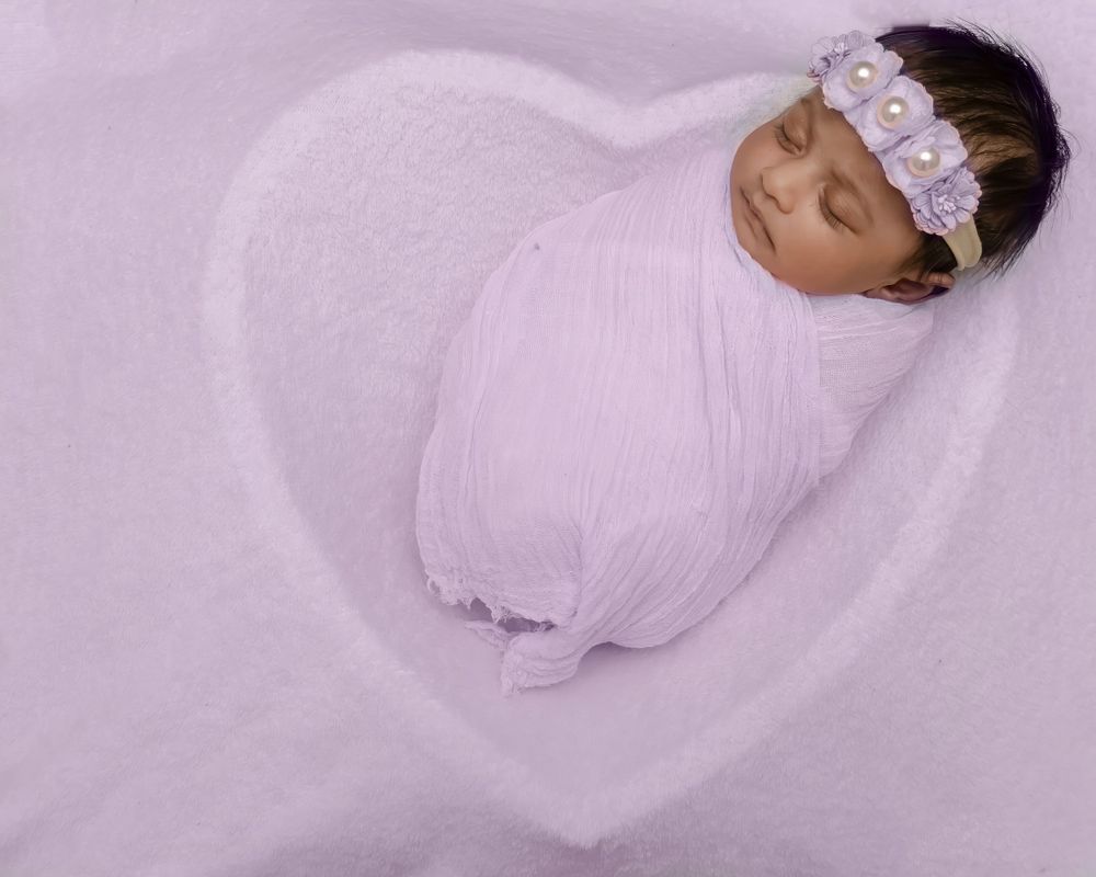 Newborn wrapped in soft pink swaddle resting on heart-shaped blanket.