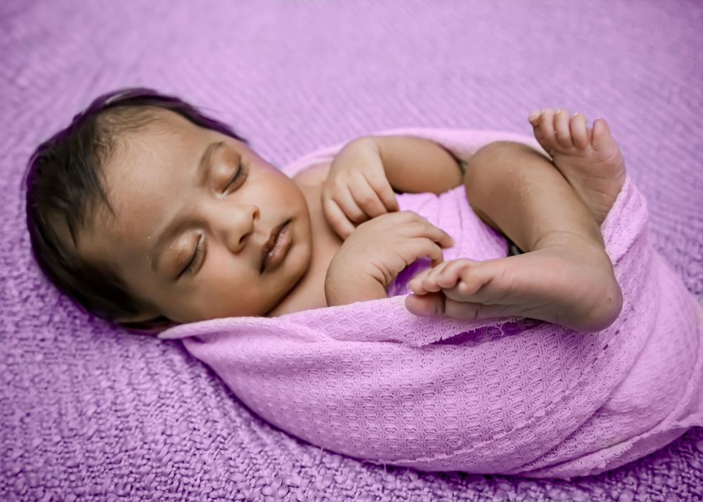 Peaceful sleeping baby wrapped in purple textured blanket.