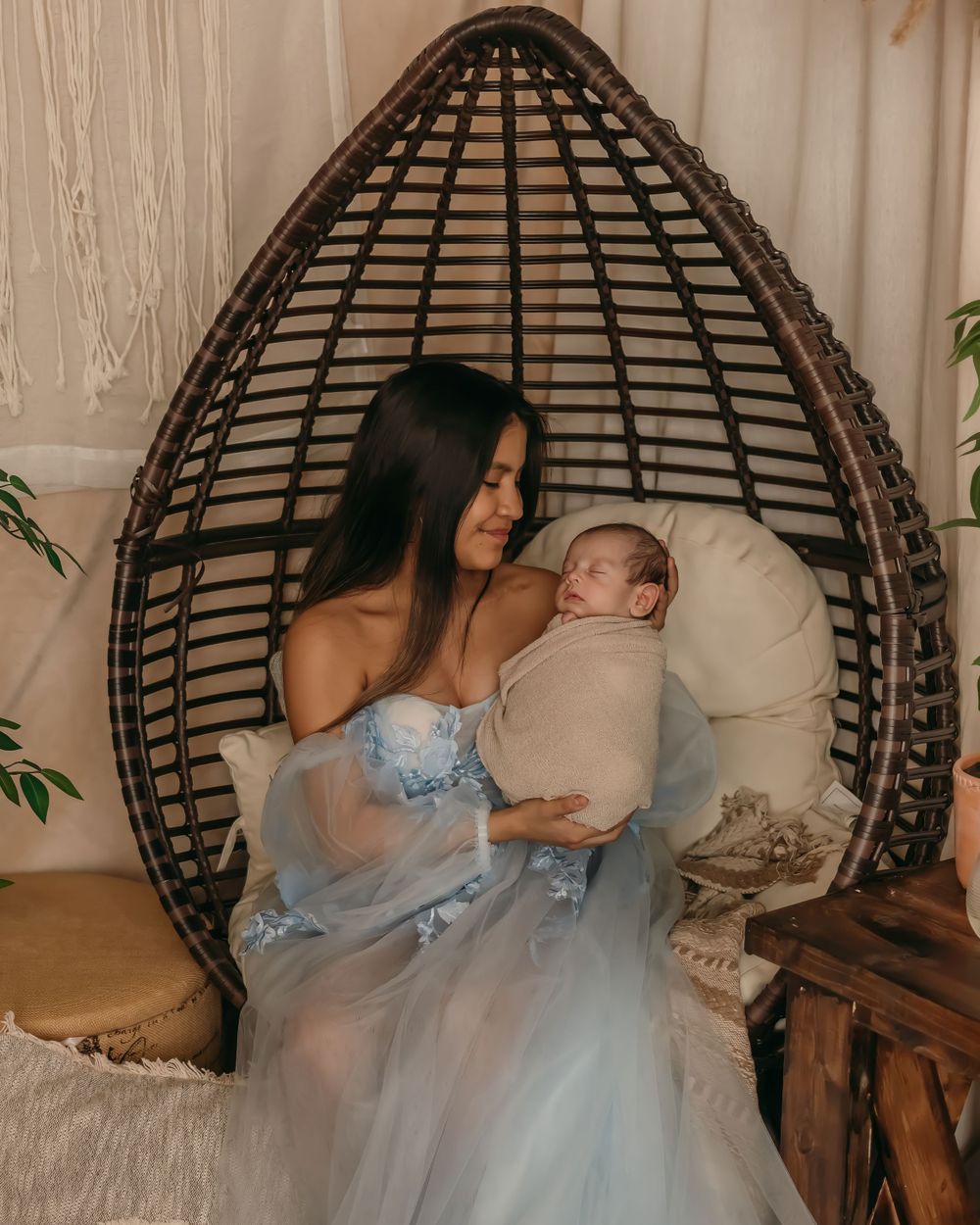 Intimate portrait in egg chair showing tender maternal moment in ethereal blue dress.