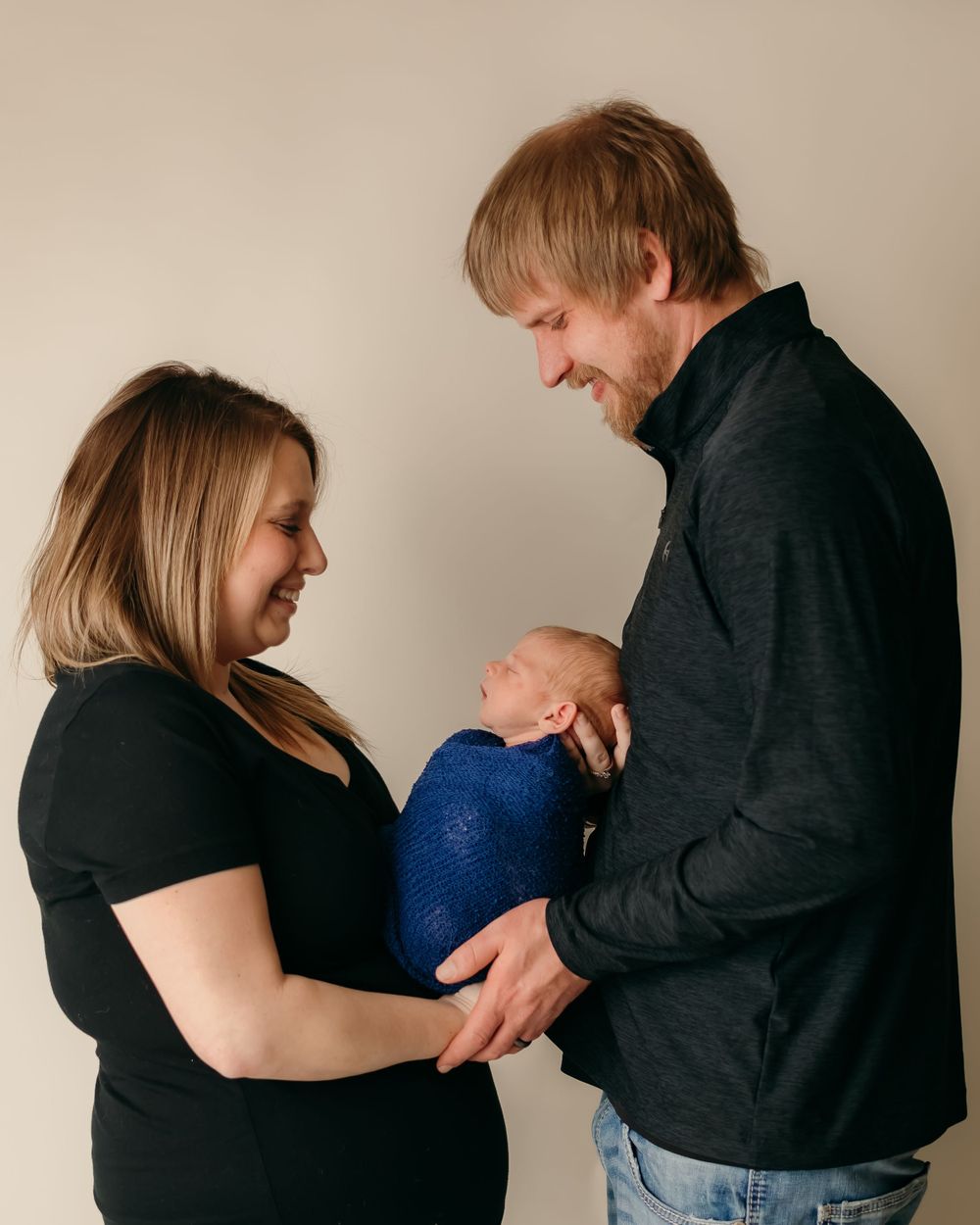 Candid moment of parents smiling while holding their swaddled baby.