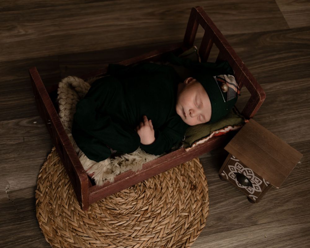 Sleeping baby in black outfit resting in wooden cradle on woven rug.
