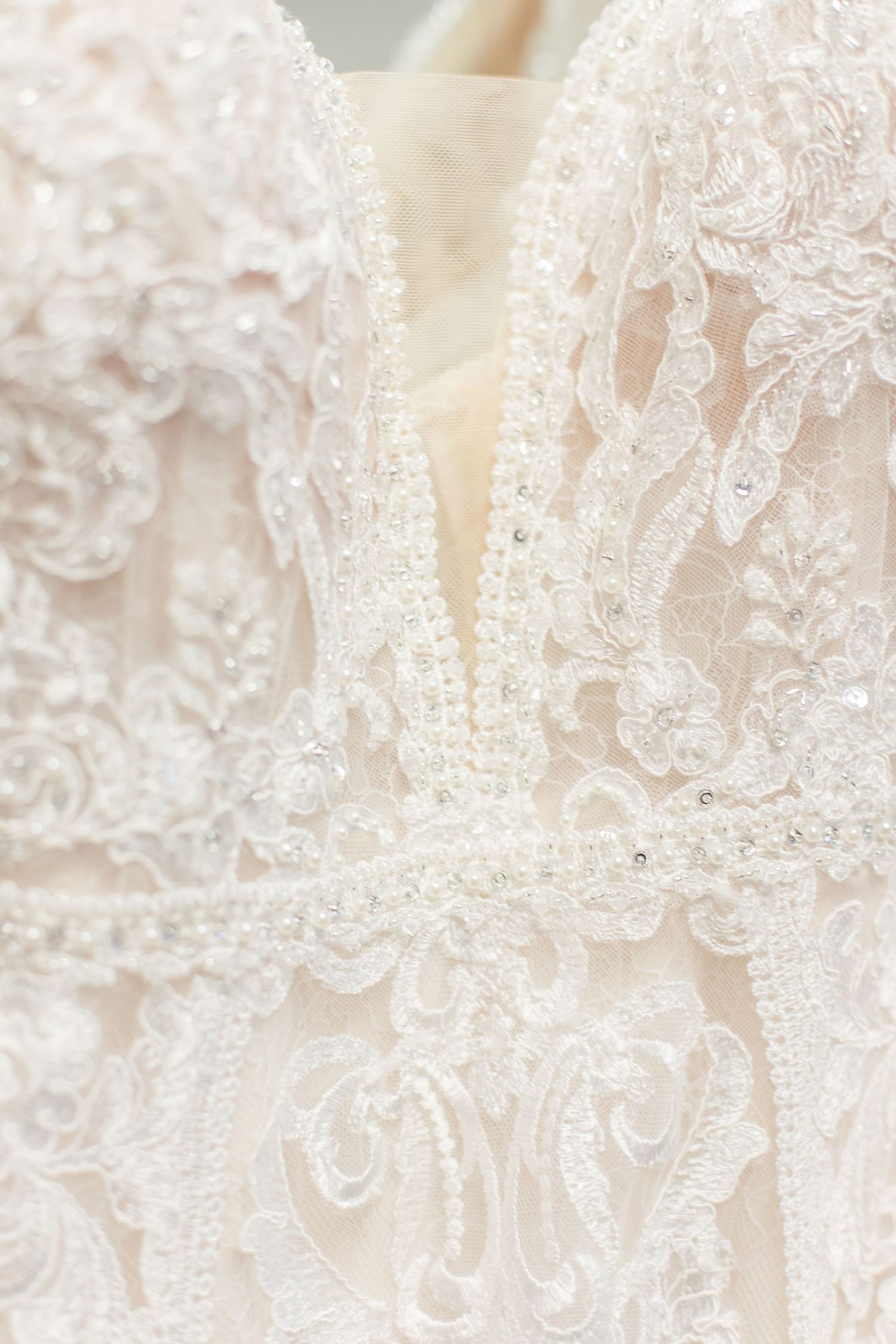 Close-up detail of delicate white lace and beadwork on a wedding dress bodice.