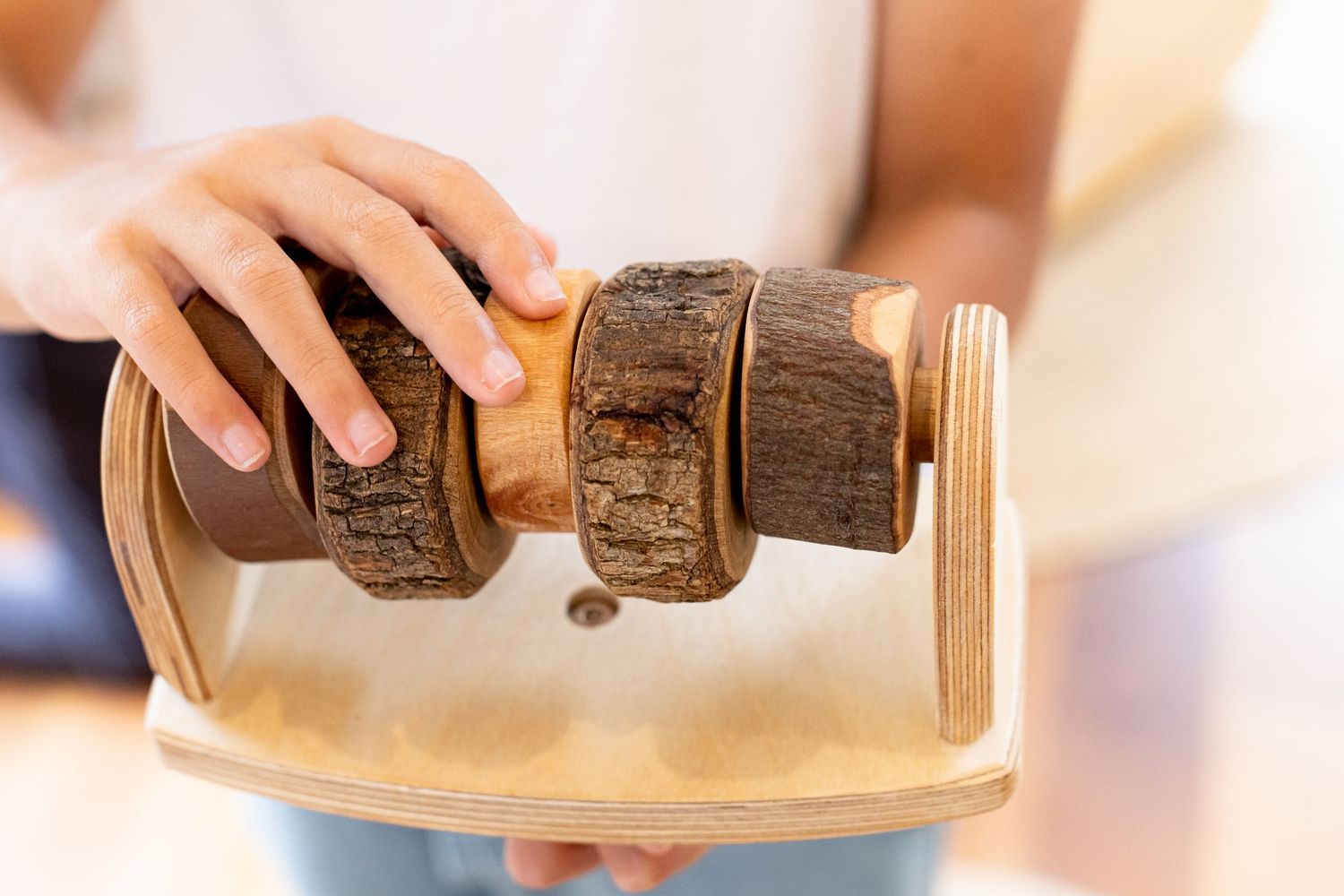 Hands holding wooden vintage-style spice grinder over light surface.