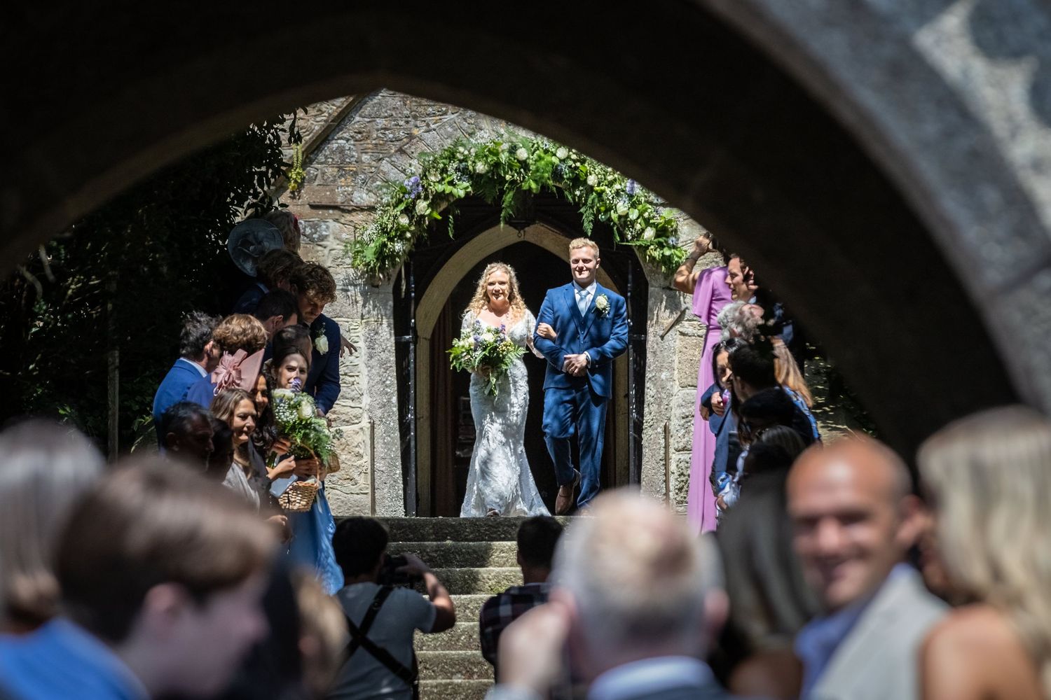 Wedding ceremony under stone archway with guests watching in natural outdoor setting.