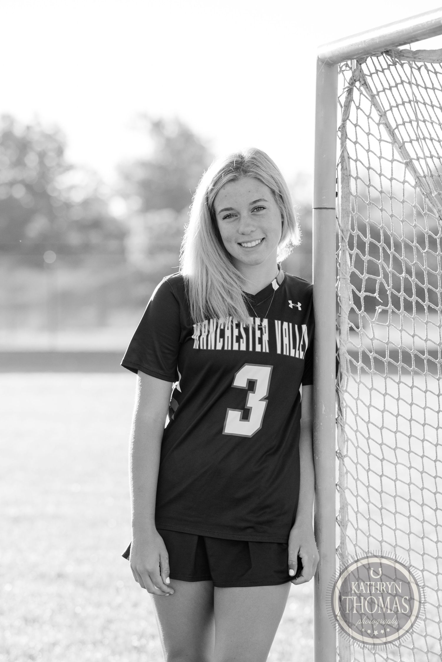 Black and white sports portrait by lacrosse goal net wearing team uniform.