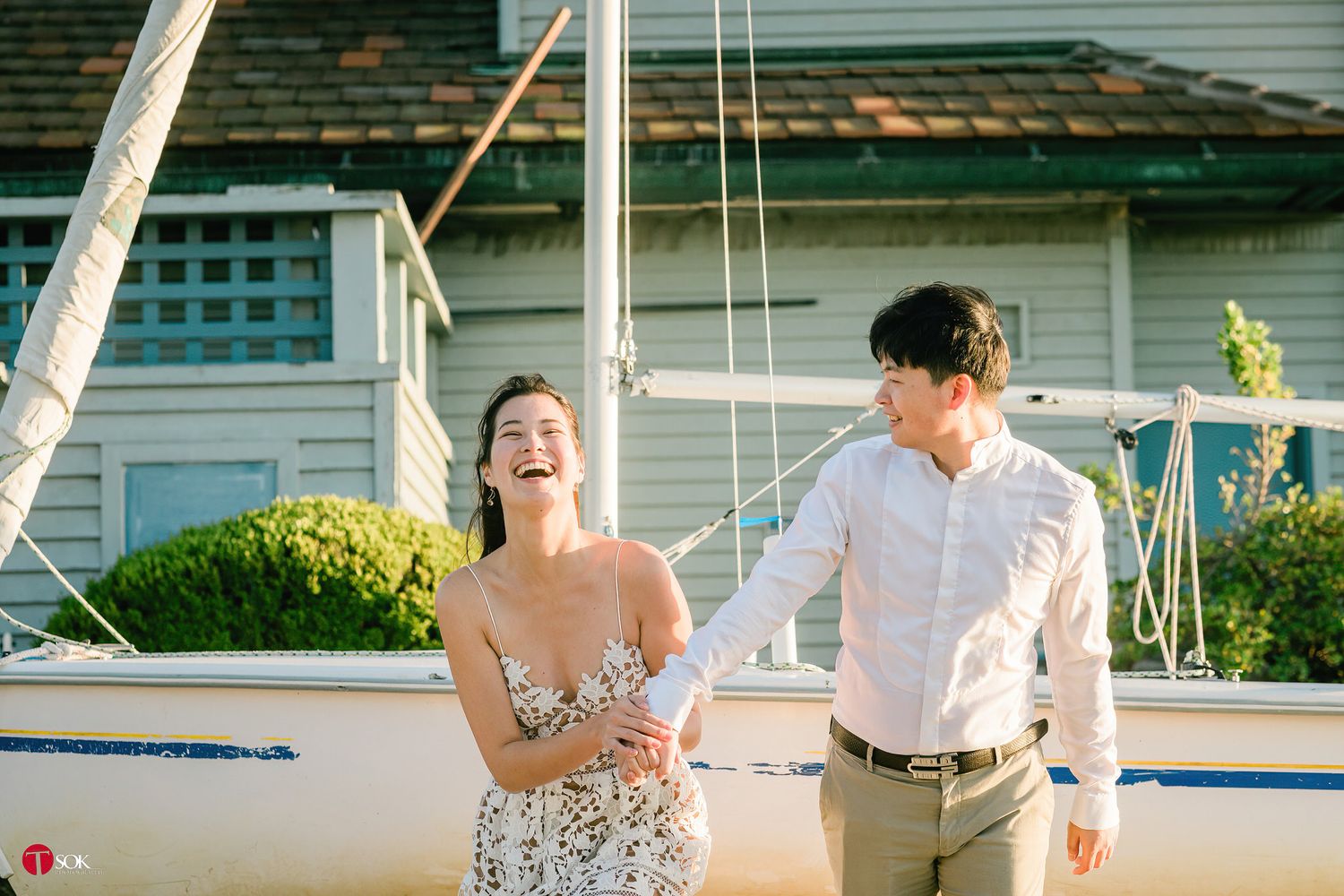A couple shares a joyful moment together beside a sailboat on a sunny afternoon.