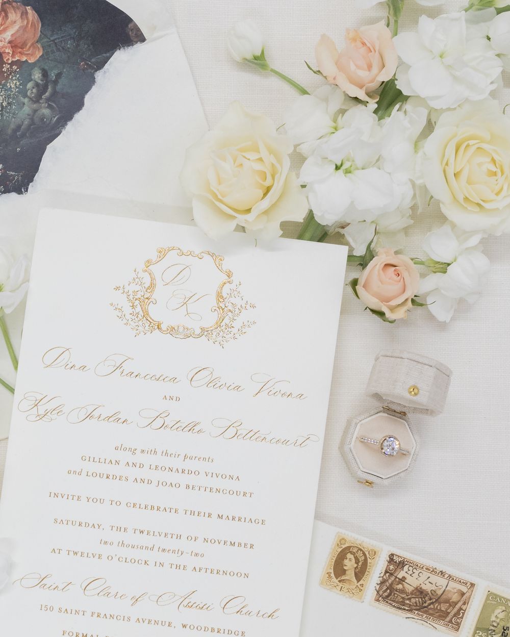 Wedding invitation with gold monogram, vintage stamps and engagement ring in velvet box.