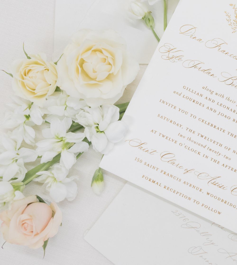 White wedding invitation with gold lettering surrounded by cream and blush roses.