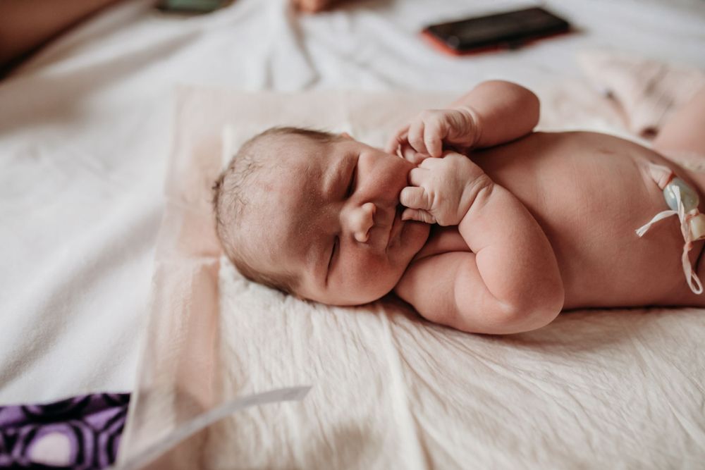 Newborn baby sleeping peacefully on white bedding while stretching tiny arms right after birth.