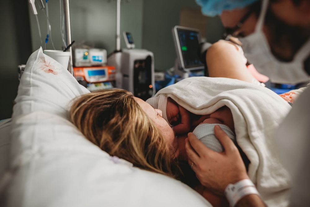 A mama in a hospital bed holds a newborn baby right after birth while medical equipment is visible in the background.