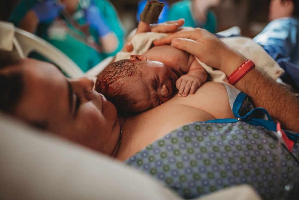 A newborn baby lies skin-to-skin on a parent's chest in a hospital setting wearing blue wristbands.