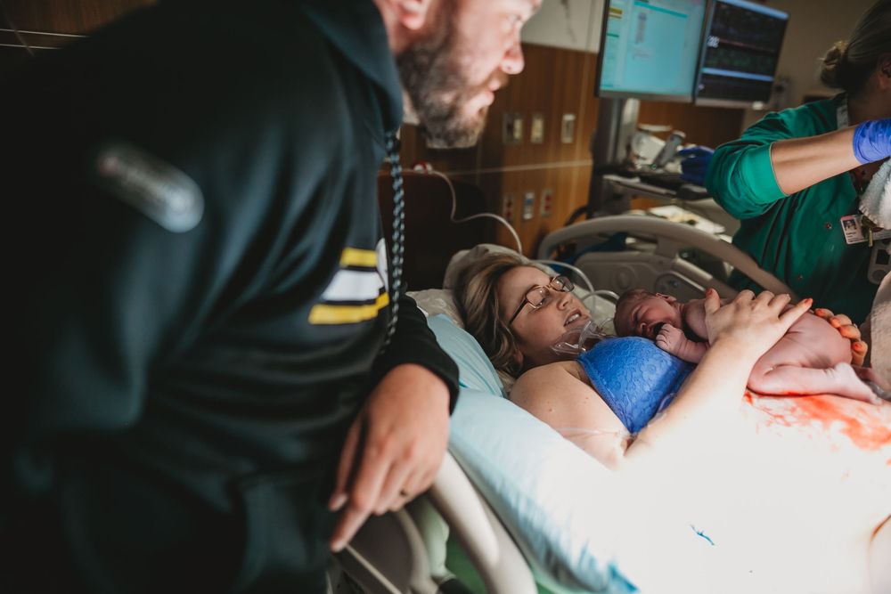 A new mama lays skin to skin with new baby as dad lovingly looks on in hospital.