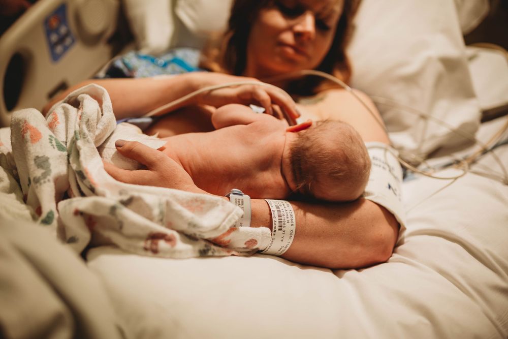 A newborn baby rests peacefully in mama's arms while being gently cradled after C-Section birth in hospital.