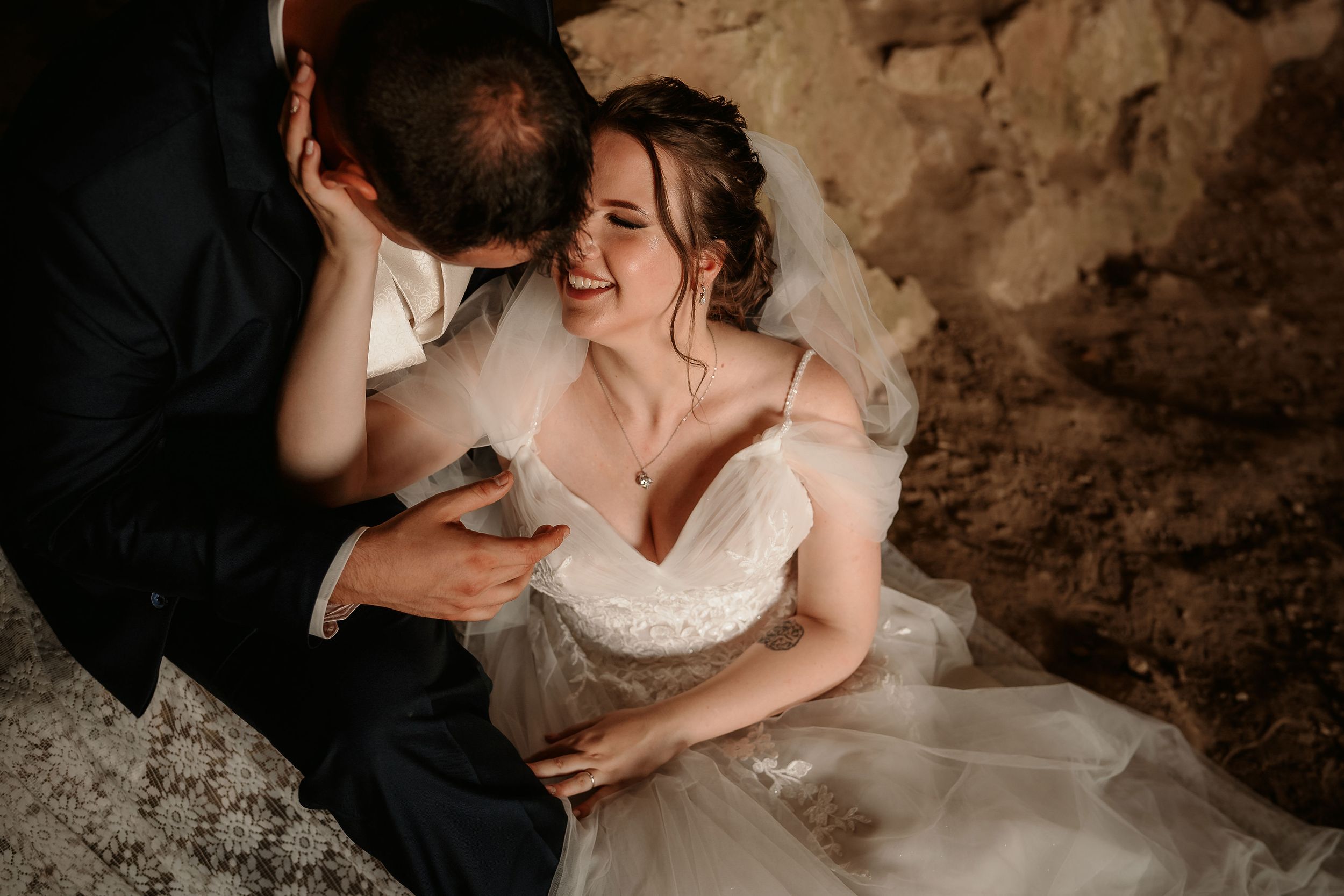 Intimate wedding couple moment captured against textured stone wall backdrop.