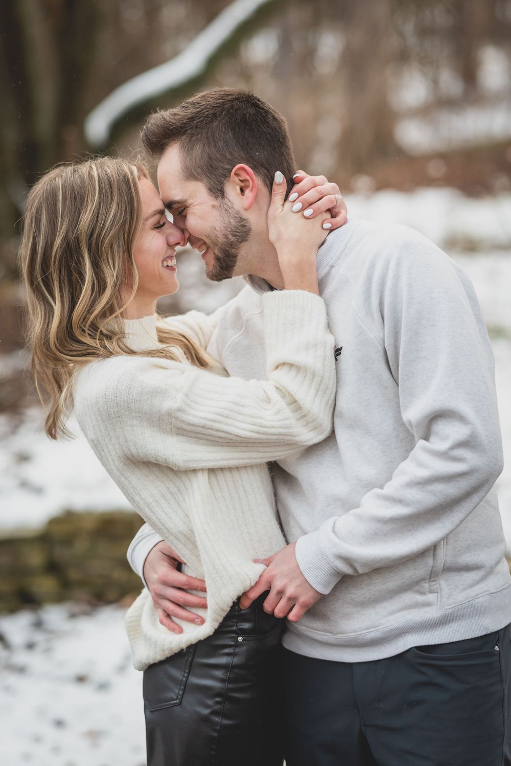 A couple in cozy winter sweaters embracing during their outdoor engagement session.