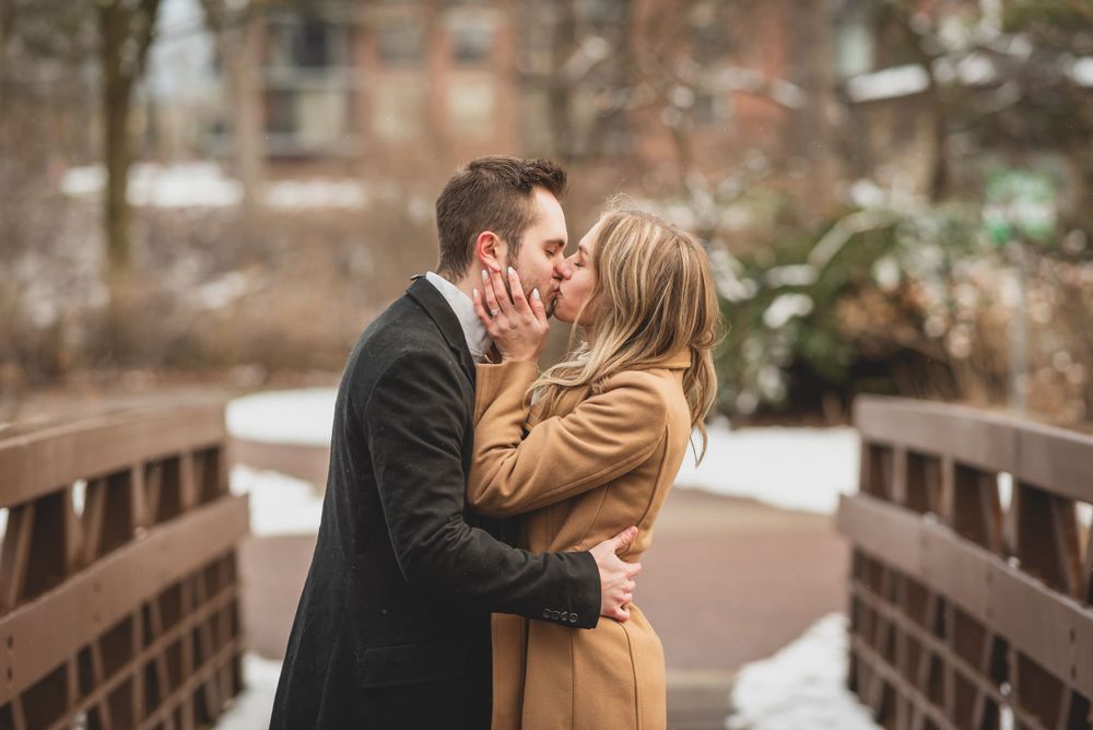 A romantic couple embraces on a wooden bridge during a winter engagement photoshoot.