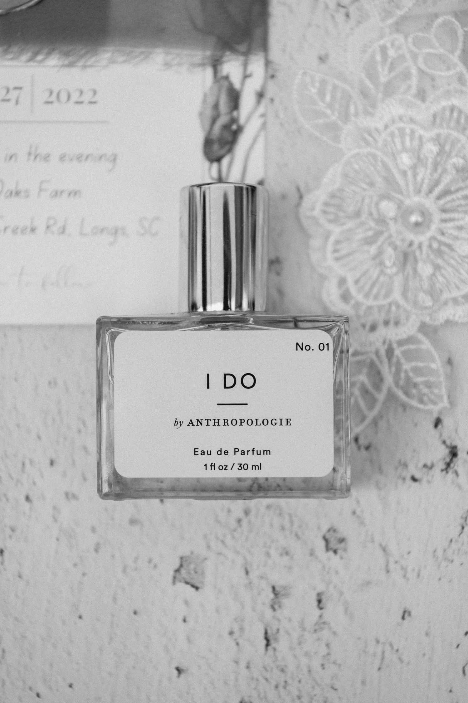 A bottle of 'I DO' perfume by Anthropologie displayed against a lace background.