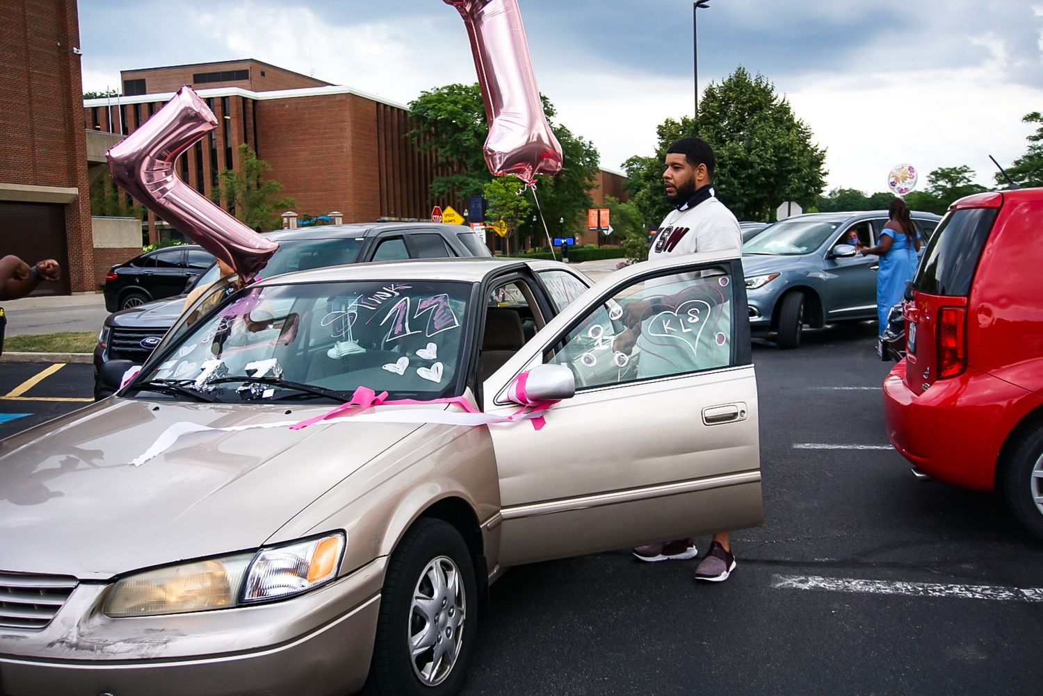 Multiple cars lined up in a parking lot decorated with pink balloons and ribbons.