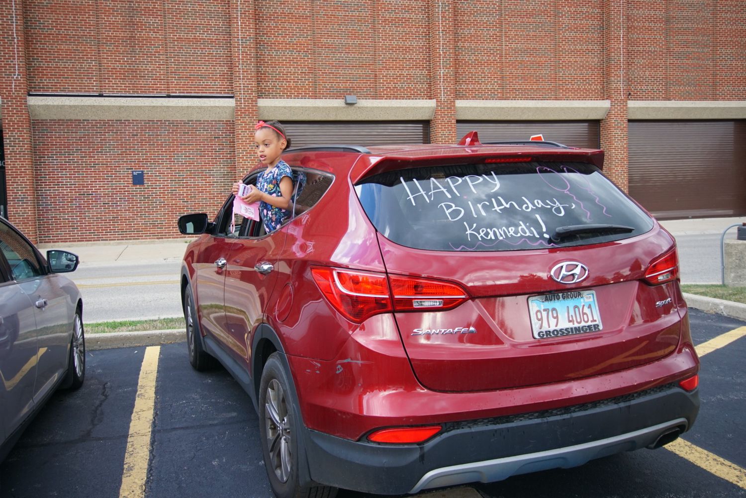 Red SUV with decorative writing on the back window parked in a brick building lot.