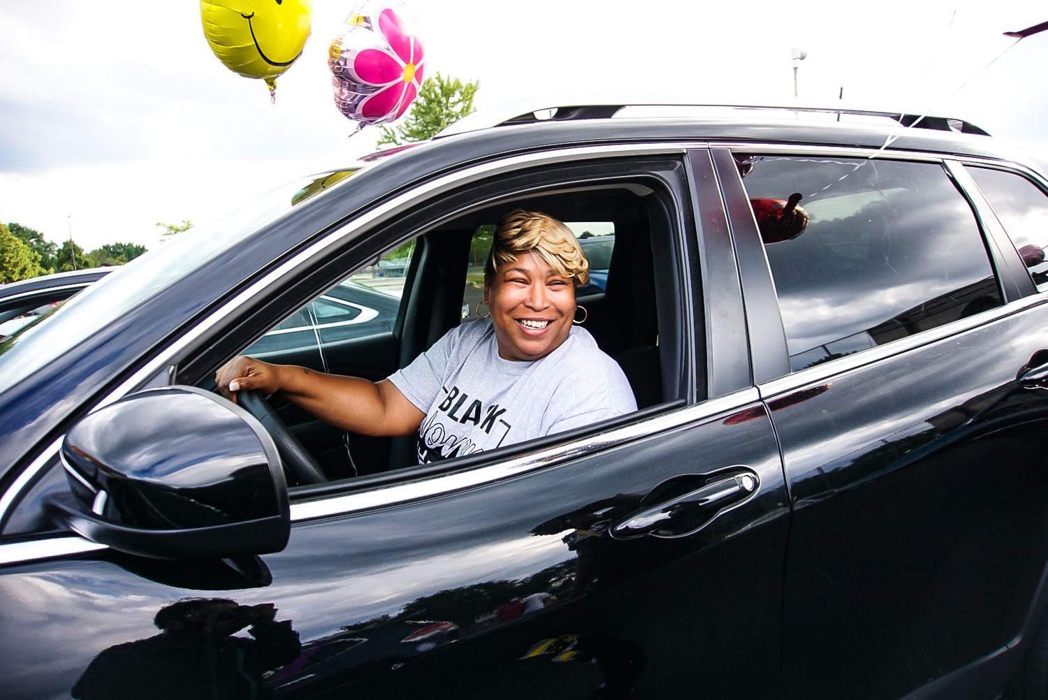 Person sitting in driver's seat of black SUV with balloons visible.