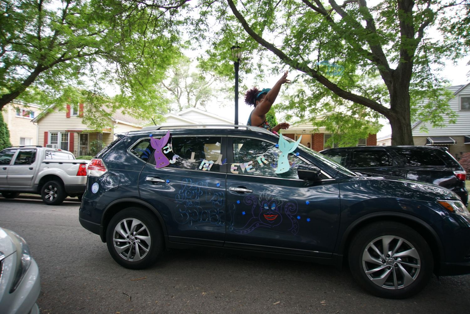 Decorated navy blue SUV with people celebrating through sunroof.