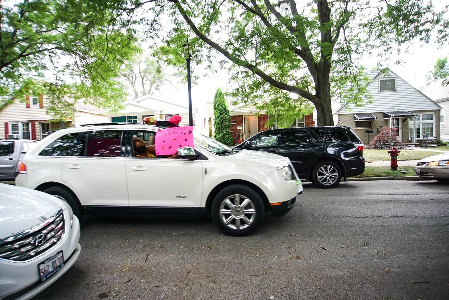 A silver SUV with pink decorations parked on a tree-lined residential street.