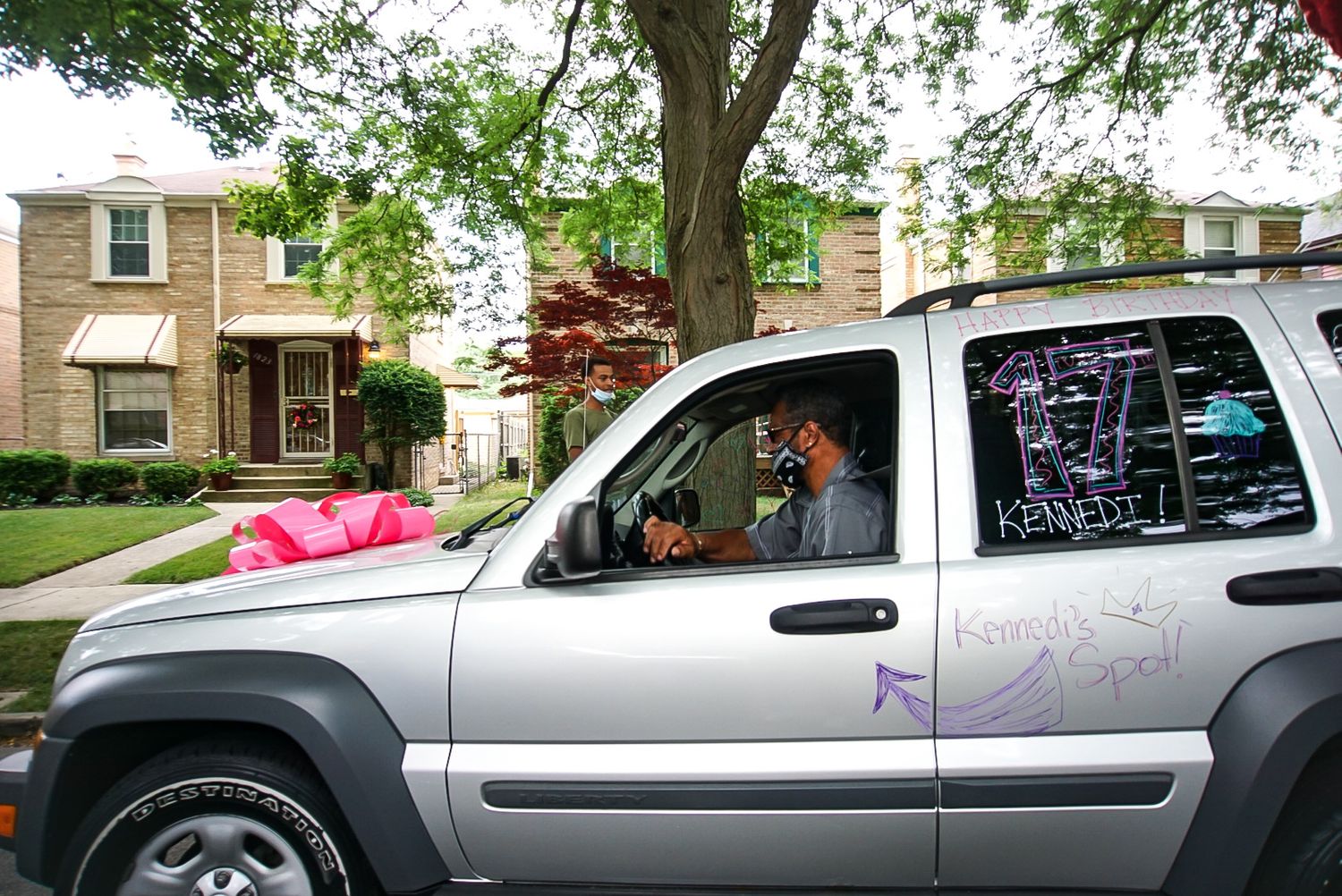 A decorated silver Jeep Liberty with pink accents parked on a residential street.