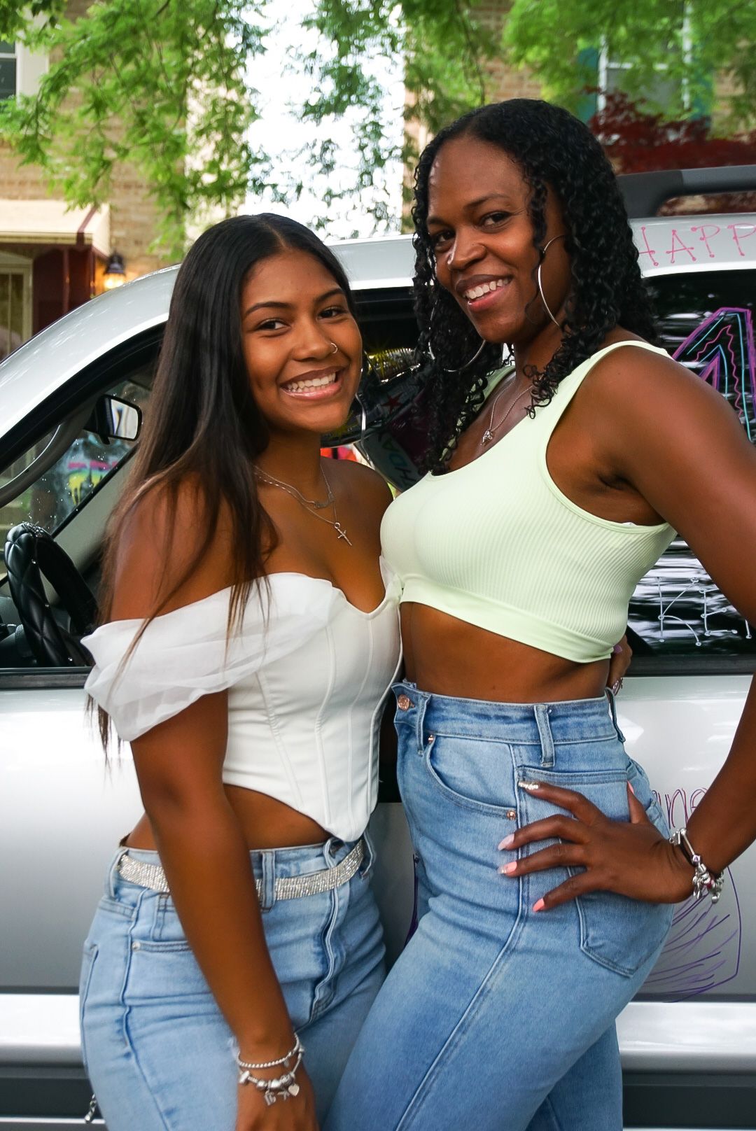 Two friends pose together in summer outfits next to a decorated vehicle.