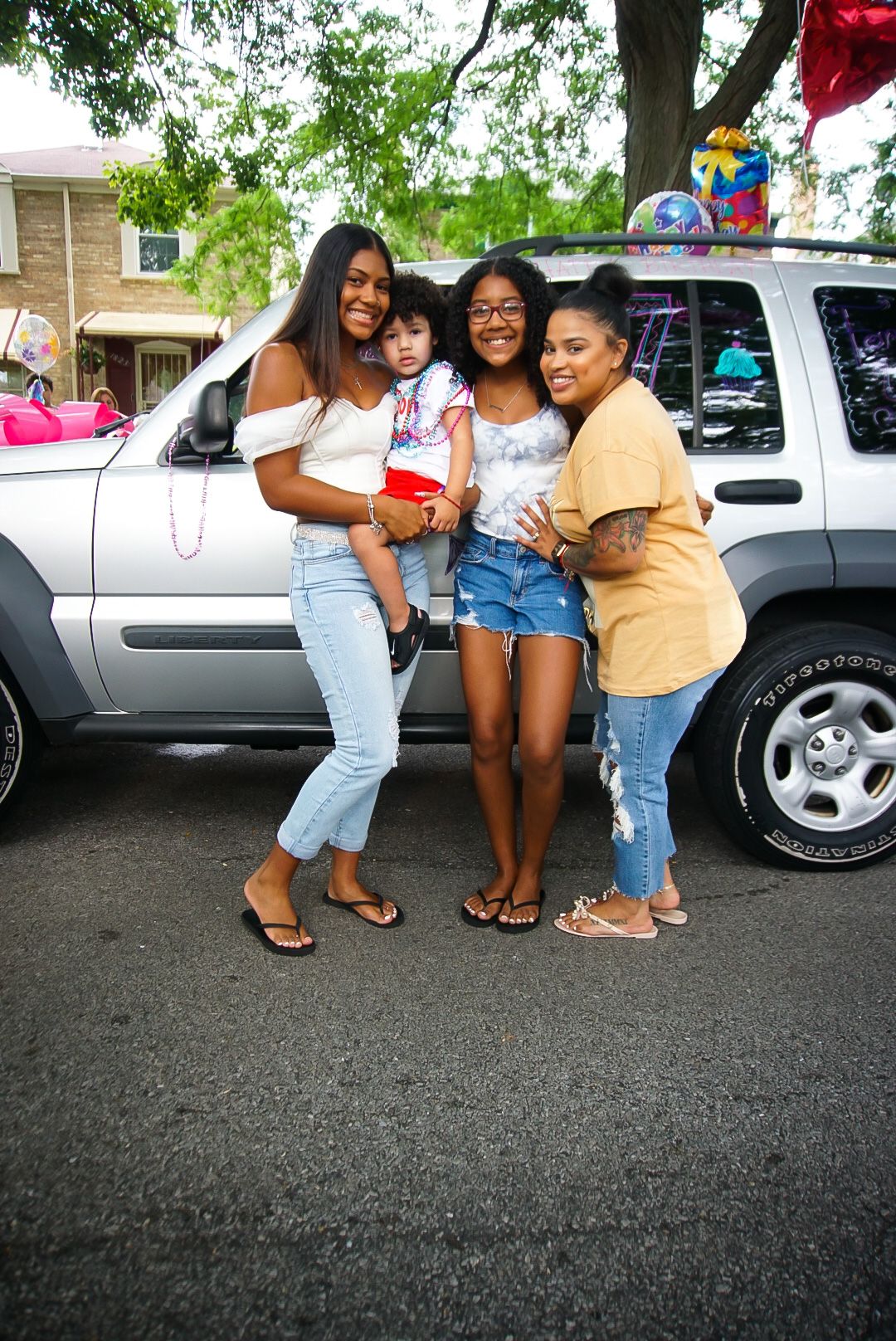 A small group poses together by a decorated silver SUV during a celebration.