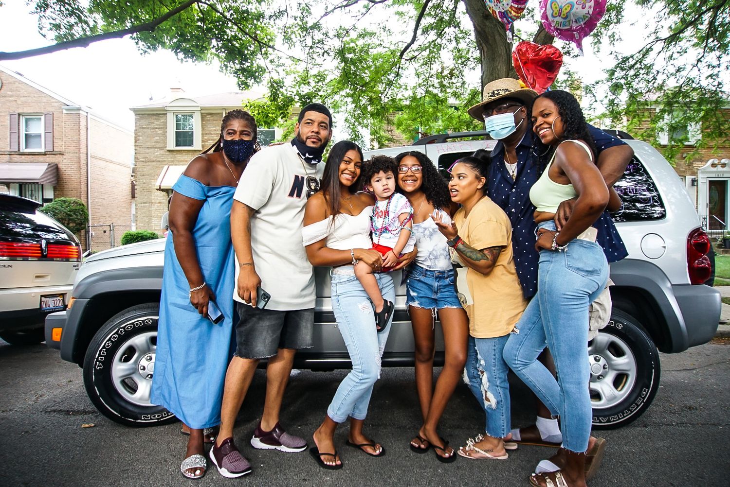 Happy group poses together outdoors by a silver vehicle during a celebration.